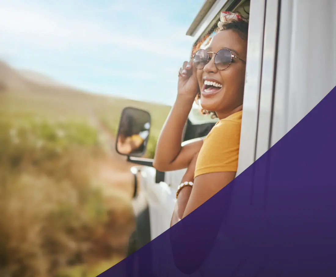 Woman leaning out of a car's driver's side window and smiling. She is wearing sunglasses.